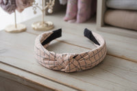 Pastel pink checkered knot headband on wooden surface, front angle