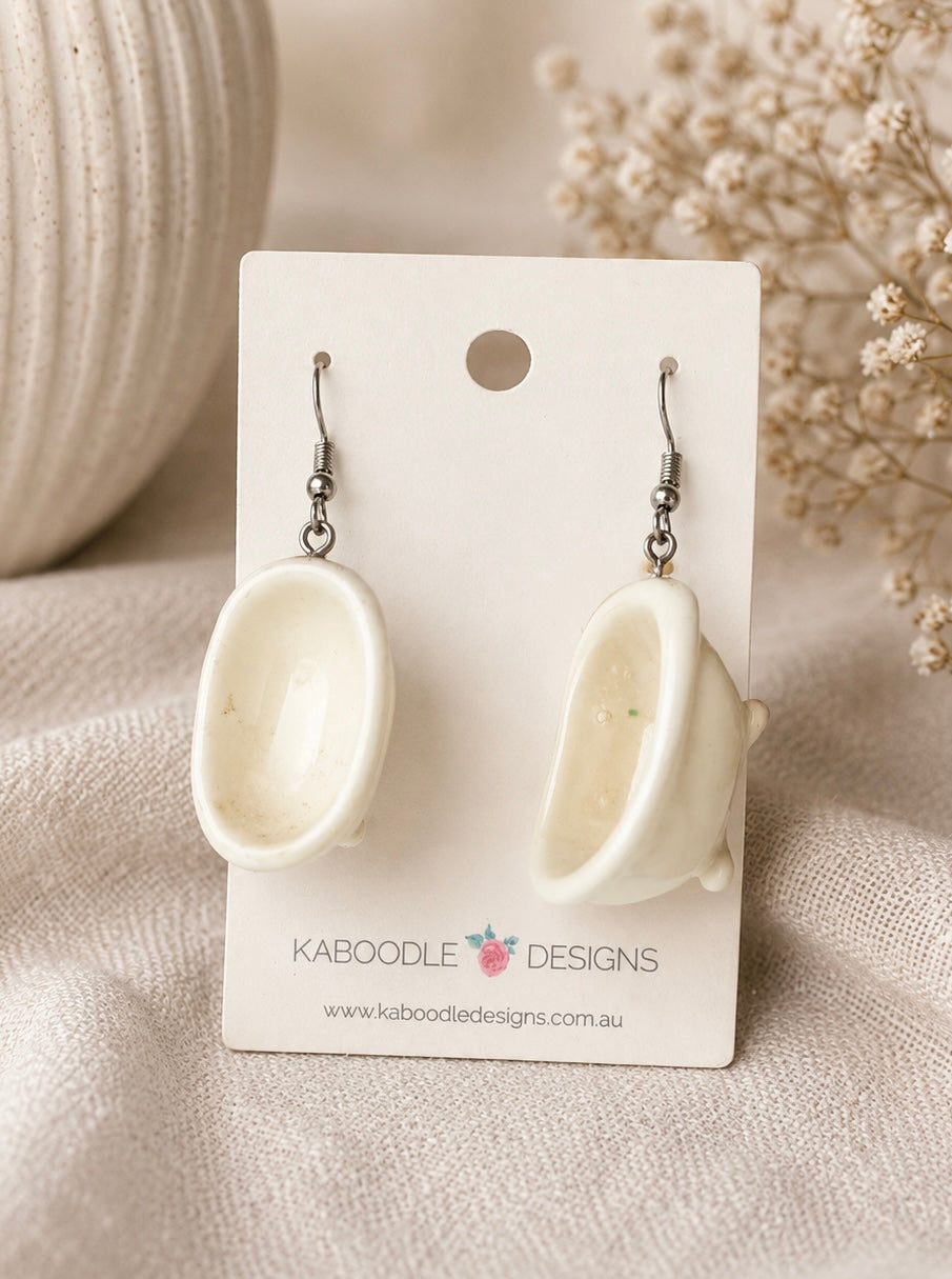 Pair of glossy white bathtub-shaped dangle earrings on a Kaboodle Designs card