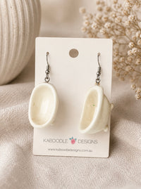 Pair of glossy white bathtub-shaped dangle earrings on a Kaboodle Designs card