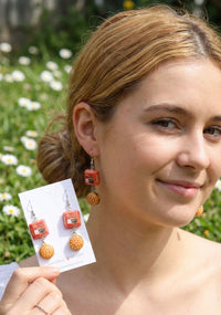 Close-up of burger drop earring worn on model's ear, showing sesame bun and layered patty detail