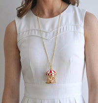 Woman wearing long gold carousel pendant necklace over white dress, close-up