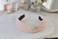 Pastel pink striped knotted headband on marble surface with vanity items in background