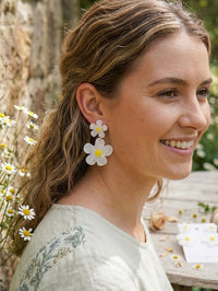 Woman wearing white acrylic daisy drop earrings with yellow centres, side profile