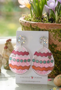 Easter egg drop earrings on card propped against a terracotta pot with spring flowers