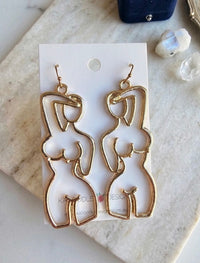 Gold-tone alloy earrings shaped as a female body outline, shown on card with two crystals nearby