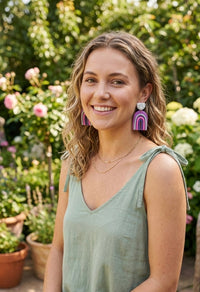 Woman wearing purple clay rainbow drop earrings outdoors, close-up on ear