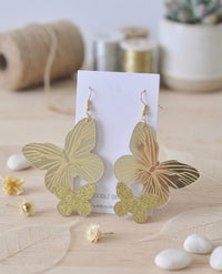 Pair of mirror-gold resin butterfly drop earrings with glitter butterfly detail, displayed on card