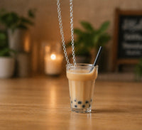 Resin boba milk tea pendant necklace hanging against a wooden table with candlelight background