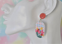 Close-up of tulip earring worn on ear showing coral stud and trellis floral drop