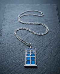Silver police box pendant necklace with blue enamel panels laid on dark slate
