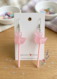Pair of pink glittery resin duck lollipop earrings on a display card with alloy hooks