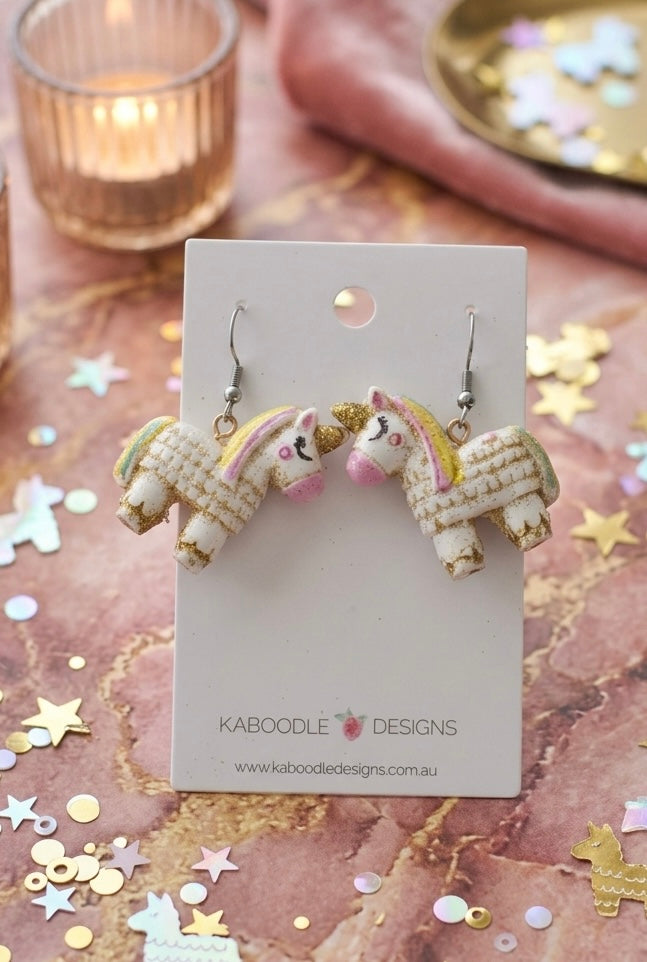 Pair of glittery white unicorn pinata resin earrings with gold and pastel detail on Kaboodle Designs card