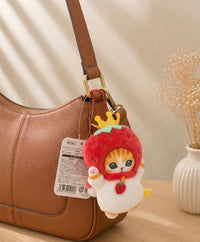 Strawberry-hooded cat plush keychain clipped onto the strap of a tan leather bag