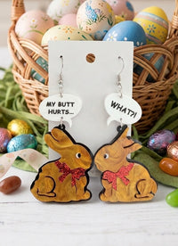 Acrylic bunny drop earrings on card with speech bubbles reading 'MY BUTT HURTS...' and 'WHAT?!', shown against an Easter egg