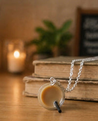 Boba pendant necklace resting on stacked books, showing pendant and silver chain clasp