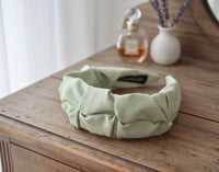 Pastel green fabric headband with ruffled texture displayed on a wooden dresser