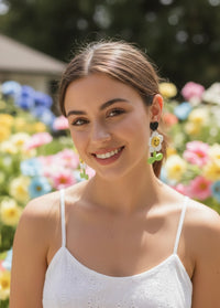 Model wearing white daisy smiley face earring with black heart stud outdoors
