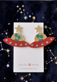 Red UFO drop earrings with gold star studs and glittery green aliens, laid flat on card