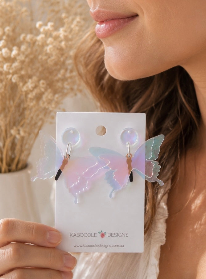 Model holding iridescent butterfly earrings near her chin, front view on card