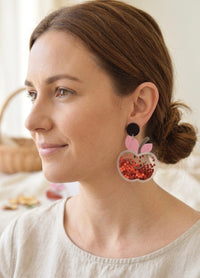 Close-up of glitter apple shaker earring worn on ear showing smiling worm detail