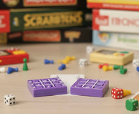 Pair of purple tic tac toe earrings laid flat on wooden surface with board game pieces