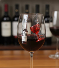 Wine bottle and glass earrings hanging inside a wine glass filled with red wine