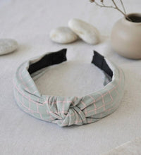 Grey and pink checkered fabric headband with centre knot on a light background