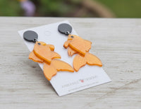 Close angled view of koi fish earrings on card resting on light timber surface outdoors