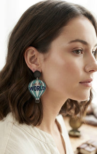 Close-up of a woman wearing a teal and white hot air balloon drop earring with black stud top