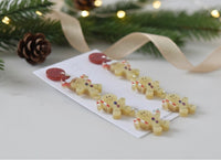 Close-up flat lay of gingerbread earrings on card beside pine sprigs, pinecone and ribbon