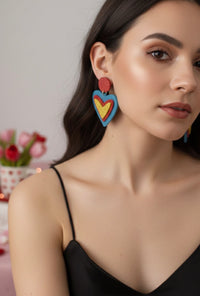 Close-up of glitter heart earring worn on model's ear showing layered blue, red and yellow design