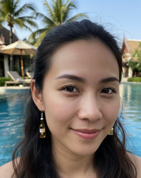 Beer bottle resin earring worn on a model's ear beside a pool