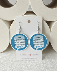 Round blue and white acrylic earrings printed with toilet roll graphic and 'I survived the toilet paper shortage of 2020'