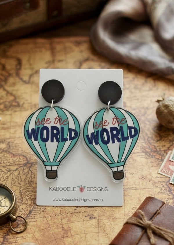 Pair of acrylic hot air balloon earrings printed with 'see the World' on a Kaboodle Designs card, styled on a map background