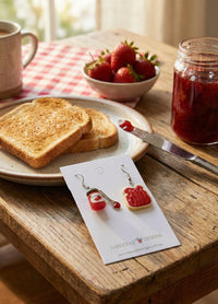 Jam jar and toast earrings styled on wooden table beside toast, jam and strawberries