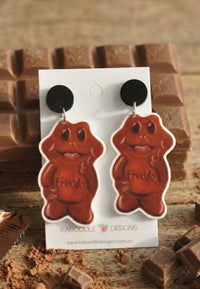 Pair of chocolate frog acrylic dangle earrings on black studs against chocolate bar background