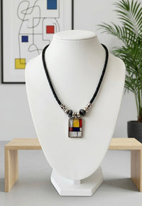 Rectangular colour-block pendant necklace with yellow, red and blue panels on a braided black cord, shown on a display bust