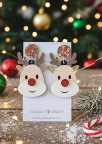 Pair of Rudolf reindeer drop earrings on a Kaboodle Designs card with a Christmas tree background