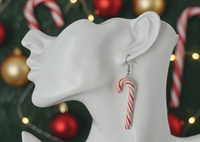 Close-up of single candy cane earring worn on ear, showing striped detail and silver hook