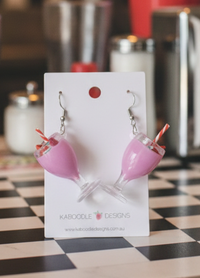 Pink watermelon milkshake earrings displayed on a Kaboodle Designs card in a diner setting