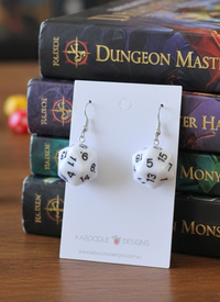 White D20 dice earrings on card displayed against stacked Dungeon Master books