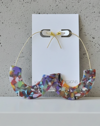 Front view of confetti terrazzo hoop earrings on card against a grey textured wall