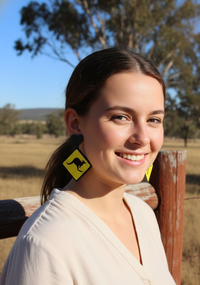 Woman wearing yellow kangaroo sign drop earring with black glitter heart top, side profile