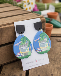 Blue teardrop acrylic earrings printed with a flower stall scene on a Kaboodle Designs card