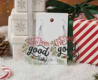 Acrylic drop earrings reading 'I've been good(ish) this year' with holly design, on card against gift boxes