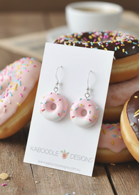 Pink resin donut dangle earrings with sprinkles on a Kaboodle Designs card, donuts in background