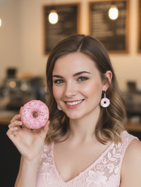 Woman wearing a single pink donut earring while holding a matching pink sprinkle donut
