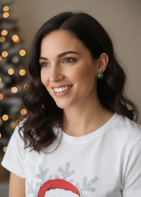 Woman wearing a green gift bow stud earring with a Christmas tree softly lit in the background