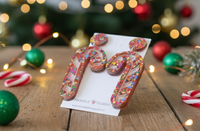 Pair of candy cane earrings displayed on card, angled view among festive baubles and candy canes