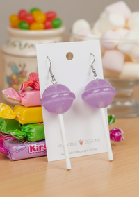 Purple lollipop resin drop earrings on a Kaboodle Designs card, with white sticks and swirl-detail candy heads